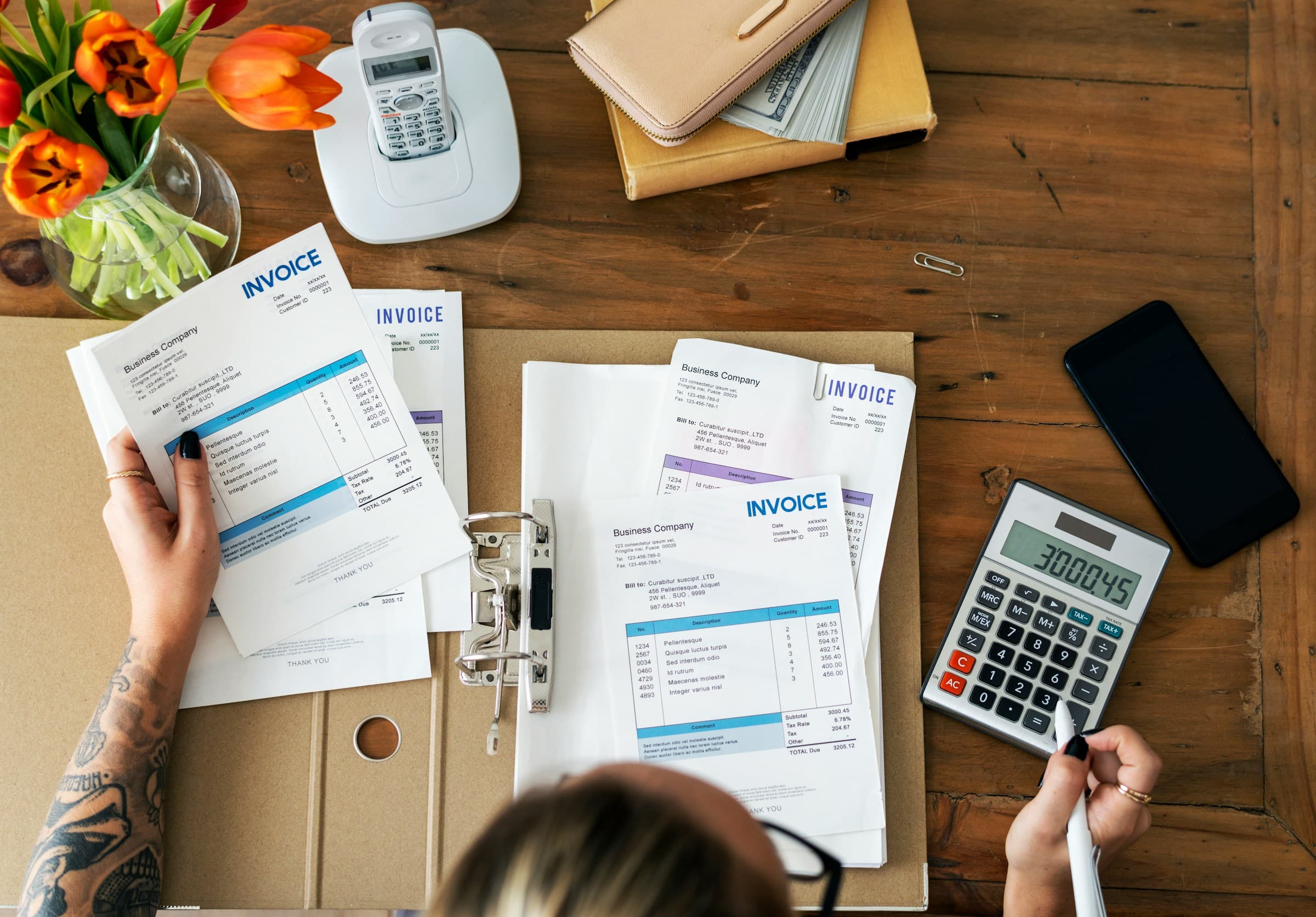 Person handling multiple invoices on a desk with a calculator on the side